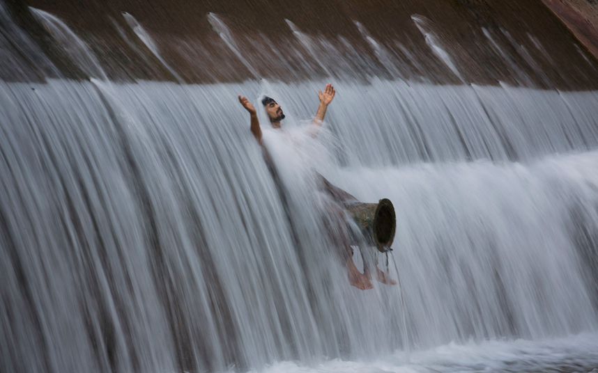 10. Житель Пакистана охлаждается в прохладной воде, стекающей поверх плотины. 