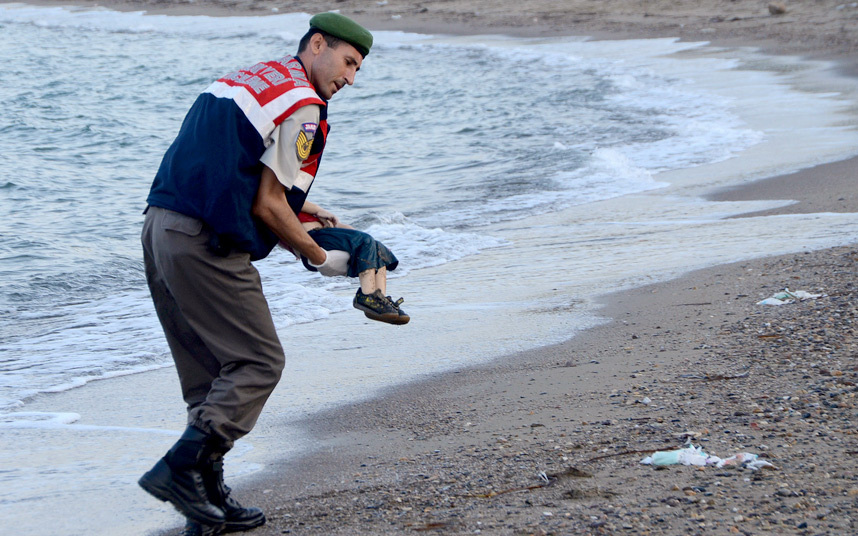 24. Турецкий полицейский несет труп утонувшего сирийского мальчика, утонувшего при попытке добраться до греческого острова Кос.