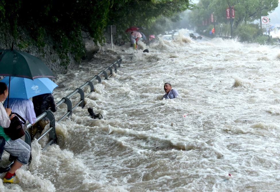 2. Мужчина пытается пробраться через мощный поток воды, вызванный тайфуном Дуджуан в 2015 в Китае.